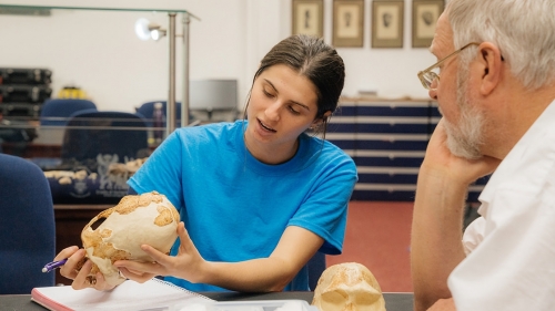a student examines part of a skeleton while a professor listens