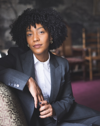 Photograph of Mary Pena. She wears a grey blazer and white button-up shirt. Photography by Katie Lenhart. 